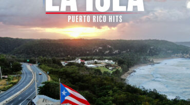 Puerto Rico flag waving at a coastal overlook with a winding road and forested hills at sunset